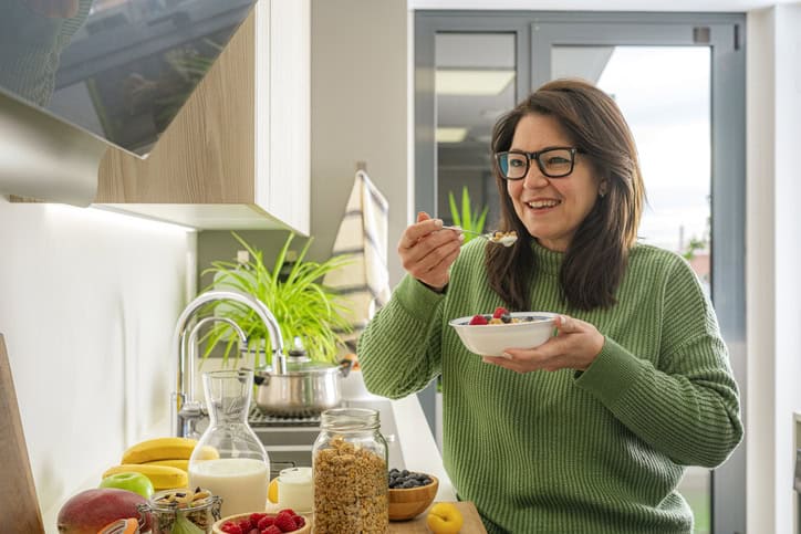 Mature woman eating a healthy snack of greek yogurt, granola and fruits in the kitchen